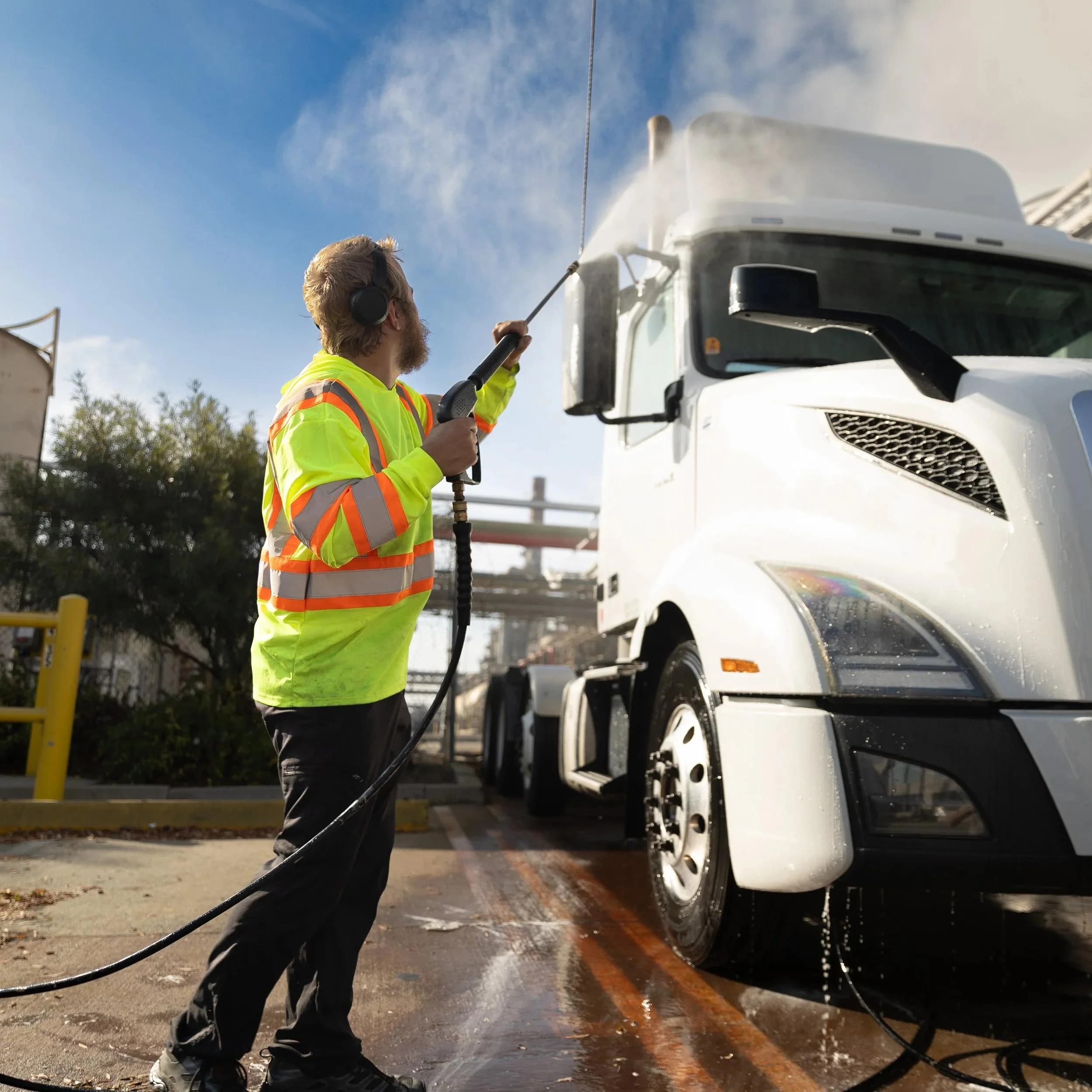 Wash technician applying the pre-rinse to a white semi-truck cab.