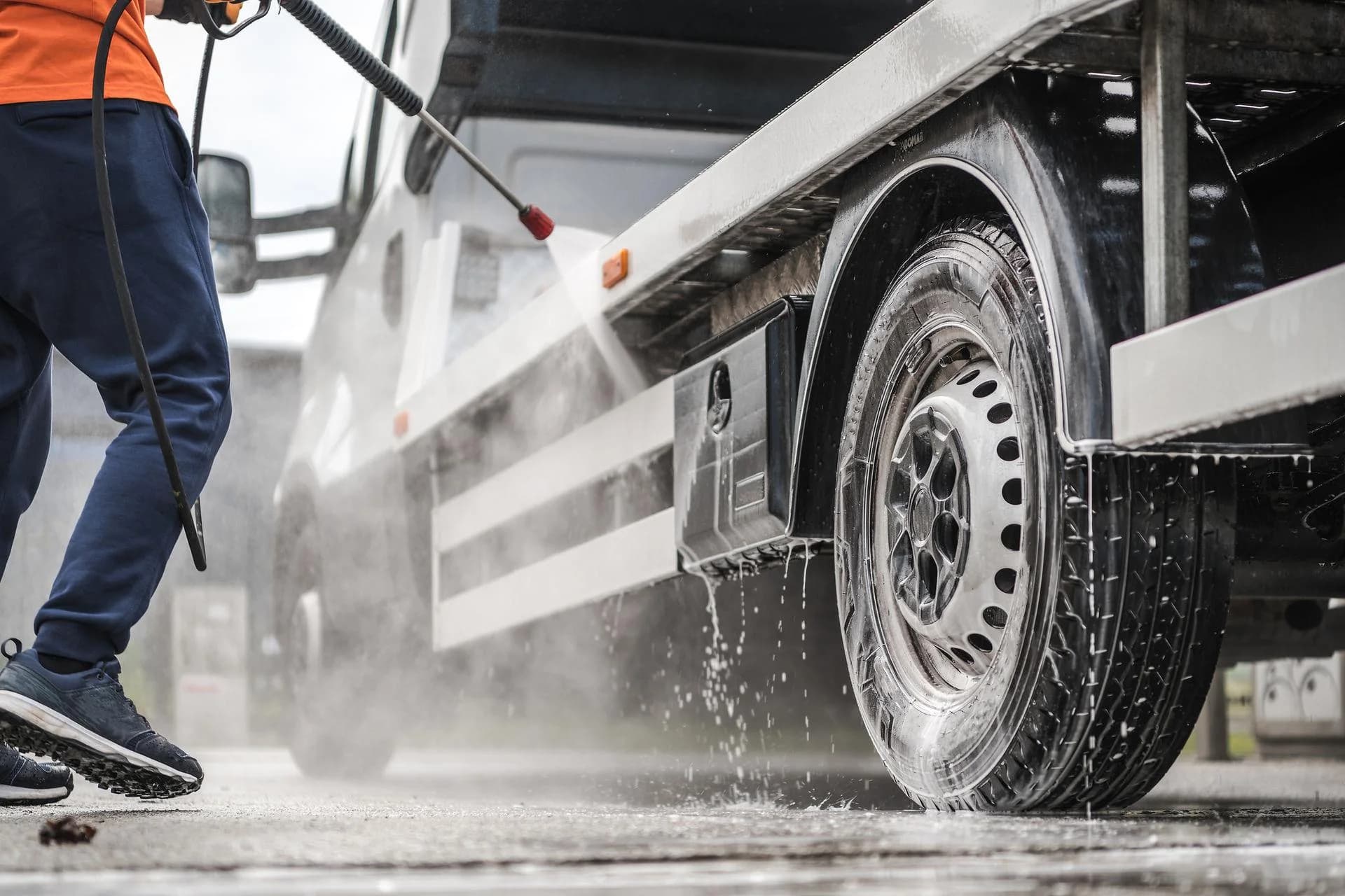 Focused rinse cleaning the wheel and lower body panels of a commercial truck.